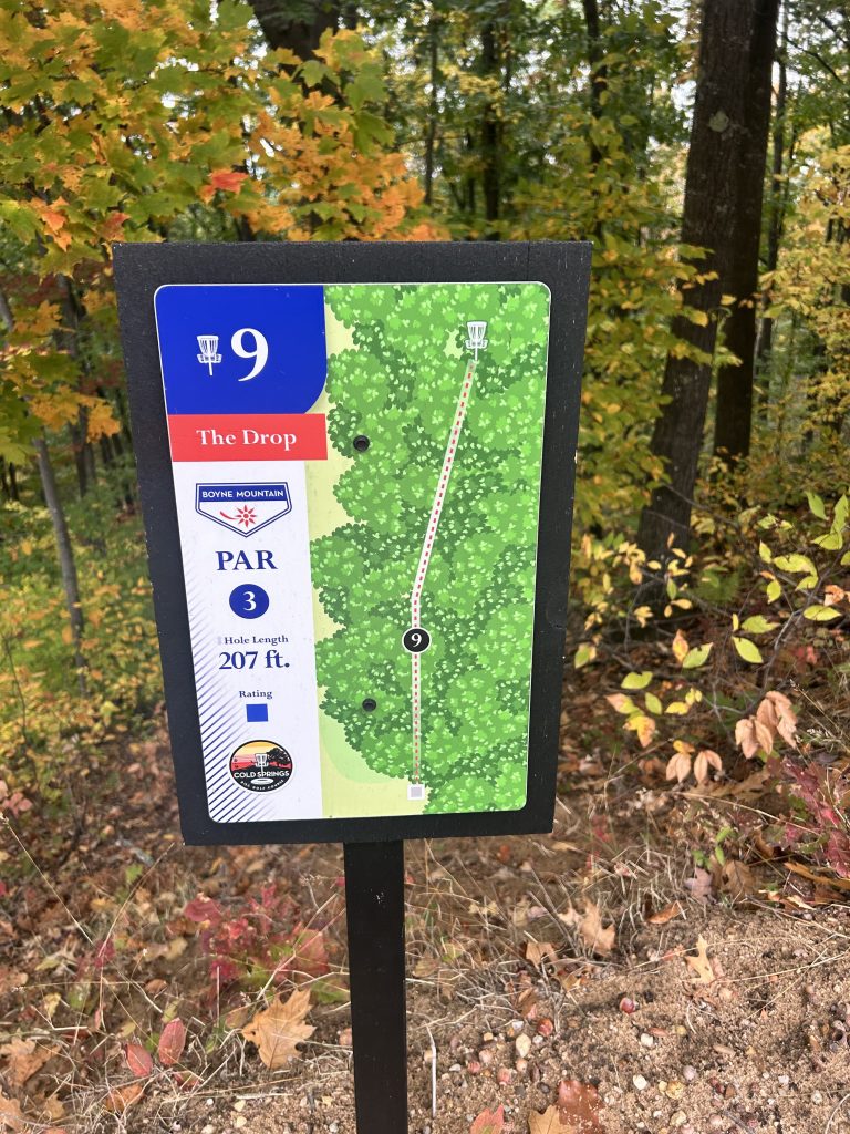 Disc golf hole sign for hole 9, titled 'The Drop'. Features a map of the hole layout, marked with a par 3 rating, a hole length of 207 feet, and surrounded by colorful autumn foliage.