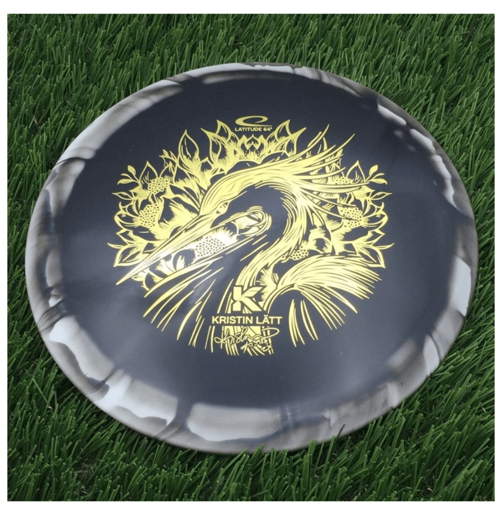A decorative disc golf disc featuring a yellow heron design and the name 'Kristin Lätt,' resting on green artificial grass.